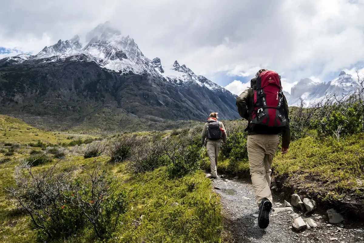 A pair of hiking poles and sturdy trekking boots on a rugged gravel mountain trail overlooking hills
